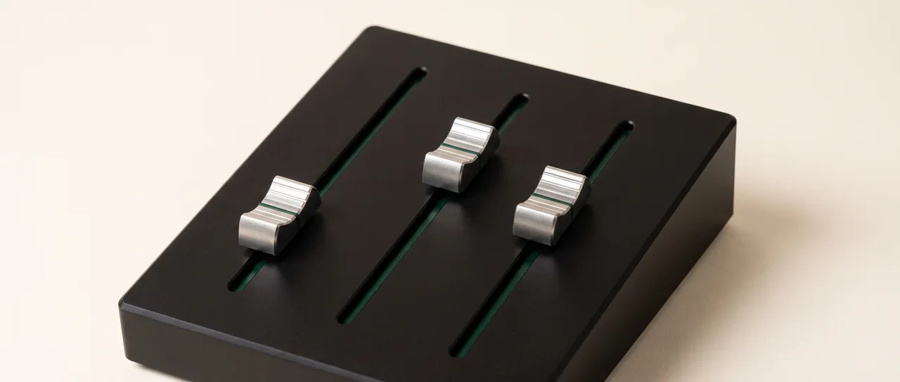 Three long-throw faders on a matte black console deck, each silver cap set to a different deliberate height.