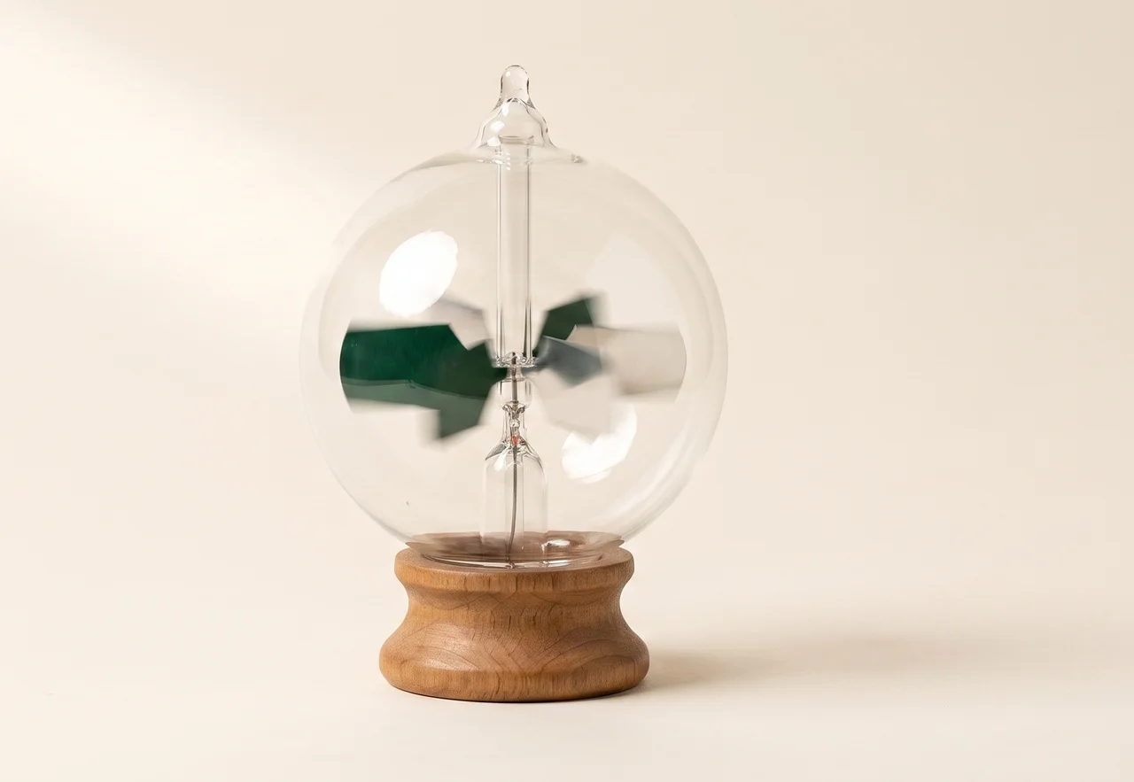 A sealed glass Crookes radiometer on a wooden base, its green and silver vanes blurred with motion as a shaft of light falls across them, with nothing attached to it.